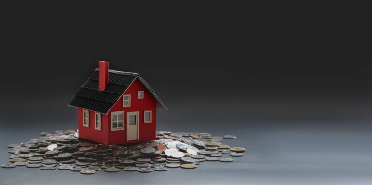 Malý červený model domu sedí na hromade rôznych mincí na tmavom gradientnom pozadí a symbolizuje investície do nehnuteľností alebo koncepty financovania bývania.