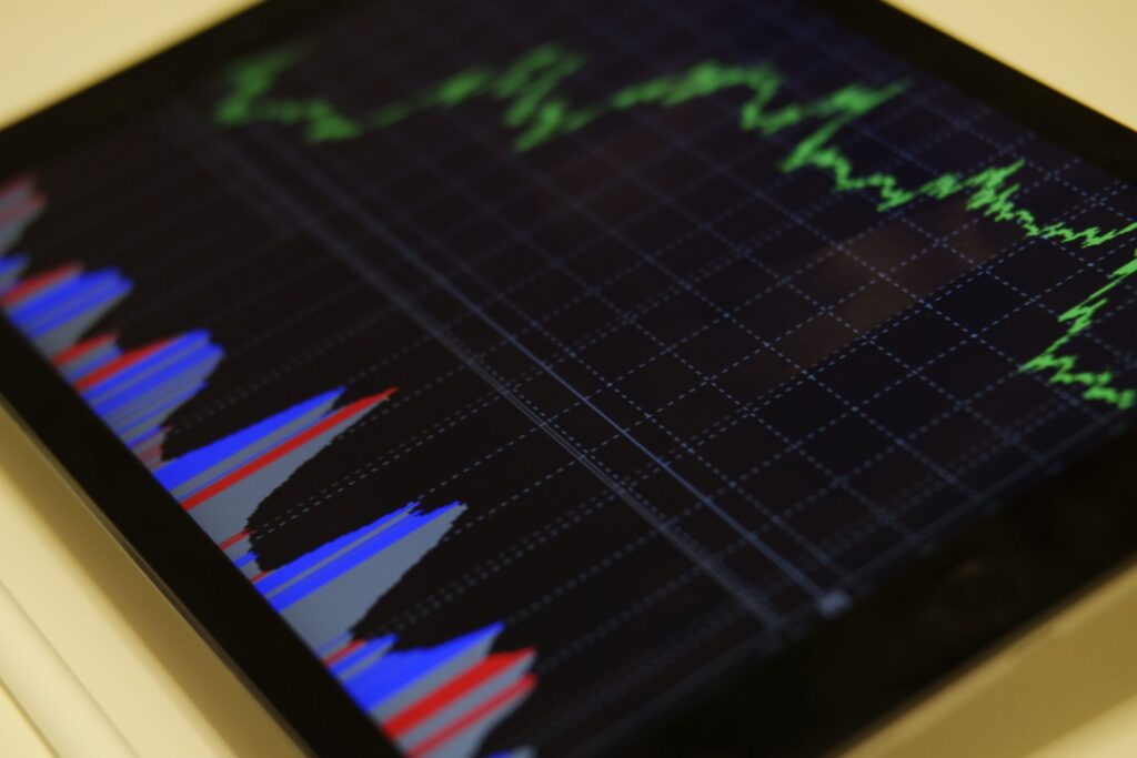 Detailný záber na obrazovku tabletu, na ktorej sa zobrazuje finančný graf so zelenými čiarovými grafmi a modrými a červenými stĺpcovými grafmi, ktoré označujú kolísajúce údaje o akciách alebo trhu a zvýrazňujú výkonnosť ekonomiky.