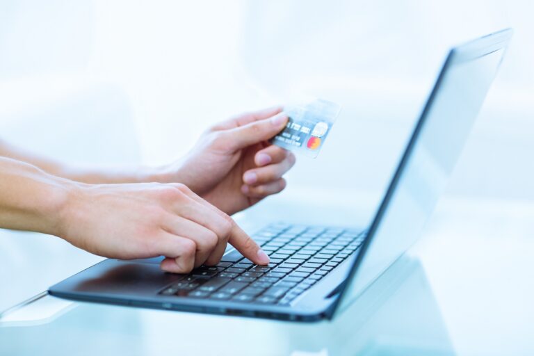Osoba, ktorá v jednej ruke drží kreditnú kartu, zatiaľ čo druhou rukou píše na klávesnici notebooku, čo naznačuje online nakupovanie alebo platbu.