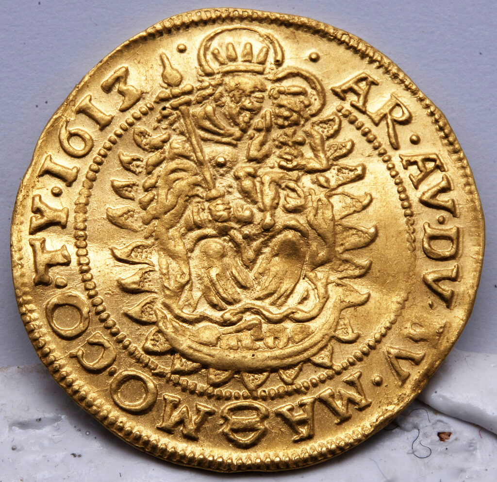 Zlatá minca z roku 1617 s reliéfom korunovanej postavy držiacej žezlo a dieťa, obklopená ozdobnými vzormi a latinskými nápismi - pozoruhodný kúsok v histórii kremnických mincovní.