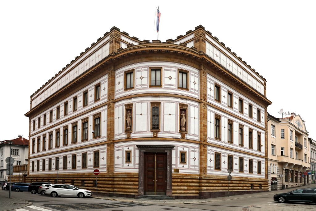 Veľká historická budova s opálenou a bielou fasádou, ozdobnými detailmi a sochami vo výklenkoch. Na streche vlaje srbská vlajka. Na ulici pred budovou je zaparkovaných niekoľko áut.
