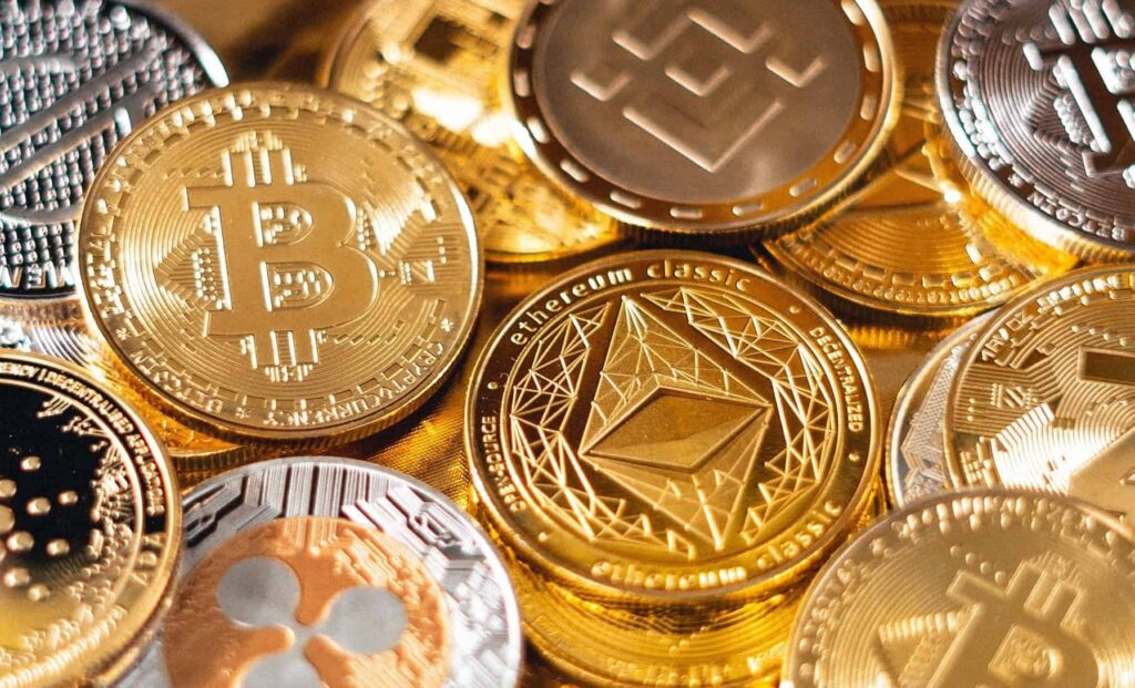Detailný záber na rôzne fyzické kryptomeny vrátane Bitcoinu, Ethereum Classic, Binance Coin, Ripple a ďalších, na ktorých sú zobrazené ich jedinečné logá a kovové vzory.