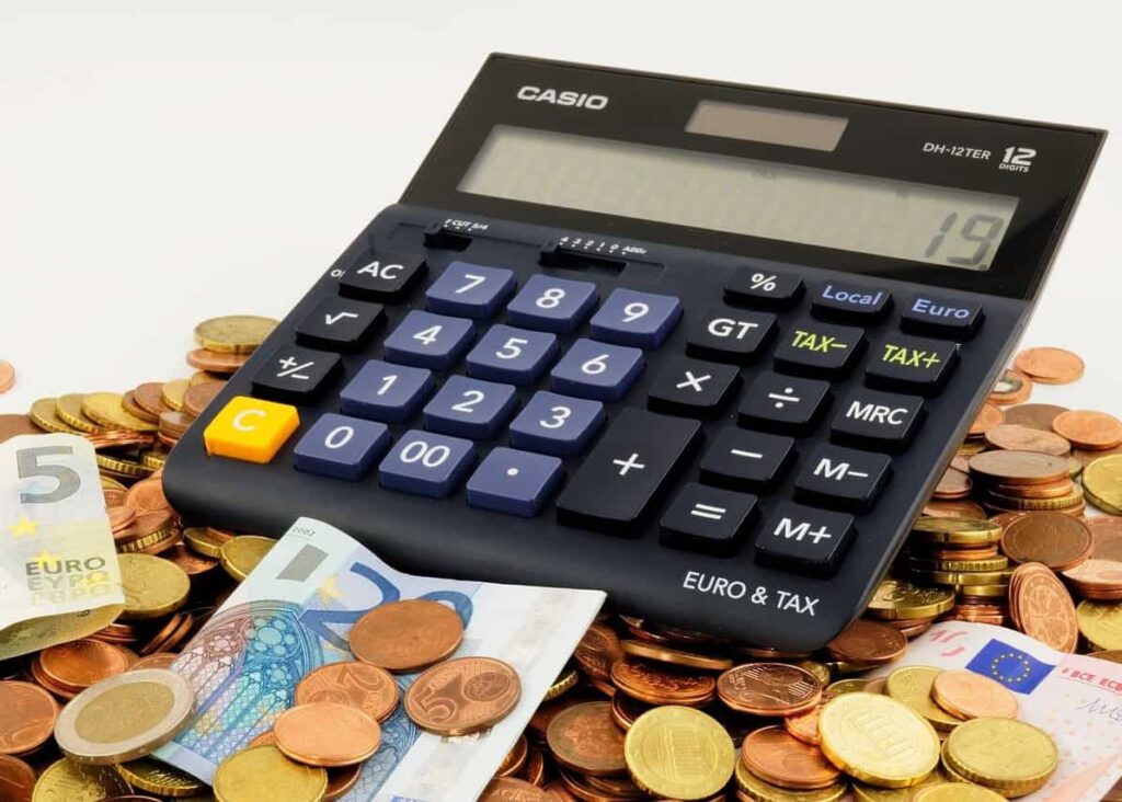 Na hromade rôznych euromincí a bankoviek leží veľká kalkulačka Casio a na jej displeji sa zobrazuje číslo 19.