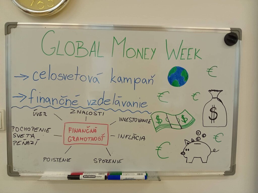 Na tabuli je zeleným písmom zobrazený Svetový týždeň peňazí, na ktorom sú nakreslené zemeguľa, symboly eura a dolára, pokladnička, hotovosť, vrecko na peniaze a rukou písané slovenské slová o finančnom vzdelávaní a témach o peniazoch.