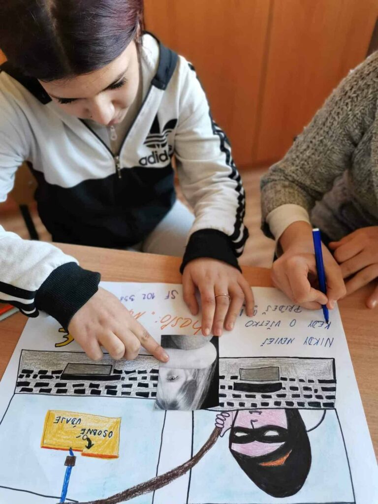 Dve deti sedia za stolom a pracujú na farebnom projekte kreslenia a písania. Jedno dieťa ukazuje na čiernobielu fotografiu na papieri, zatiaľ čo druhé drží modré pero a je pripravené písať.