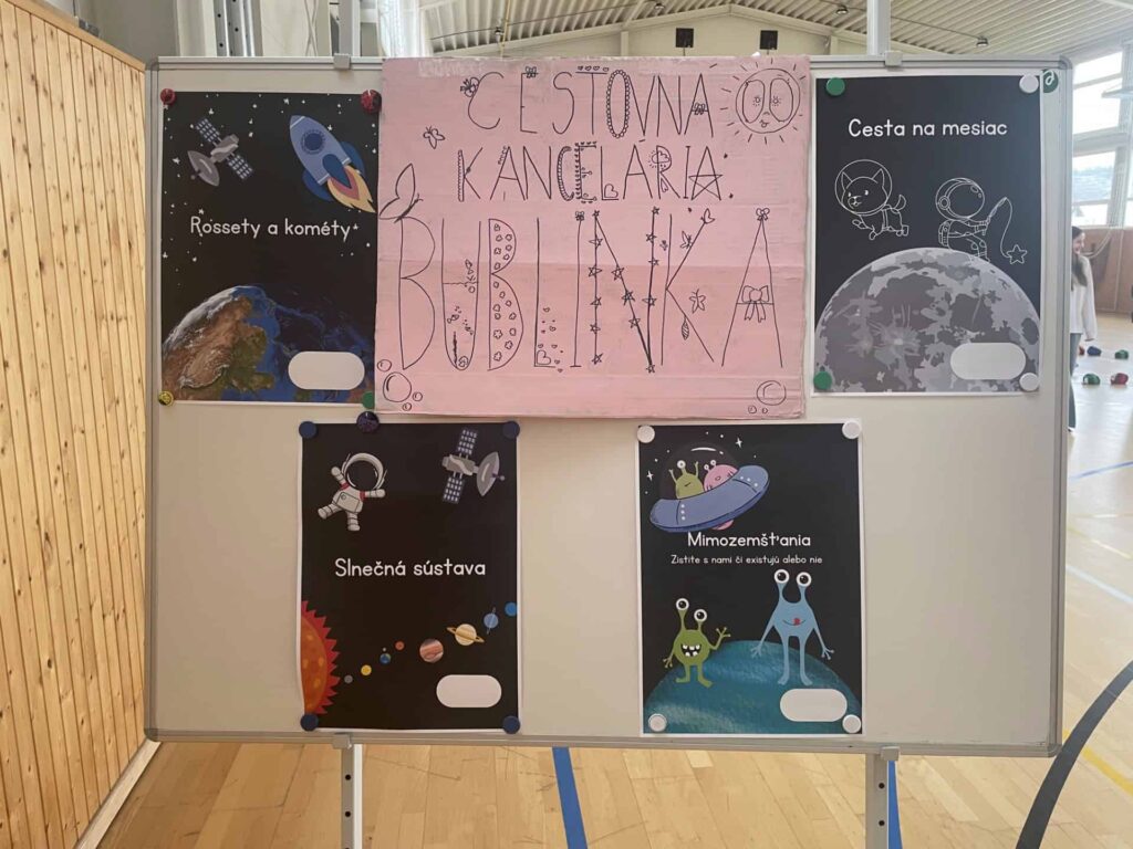 Na tabuli sú vystavené farebné vedecké plagáty o vesmíre vrátane komét, slnečnej sústavy, mimozemšťanov a Mesiaca. V hornej časti je veľká ružová tabuľa s ručne písaným textom v slovenčine, ktorú zdobia kresby.