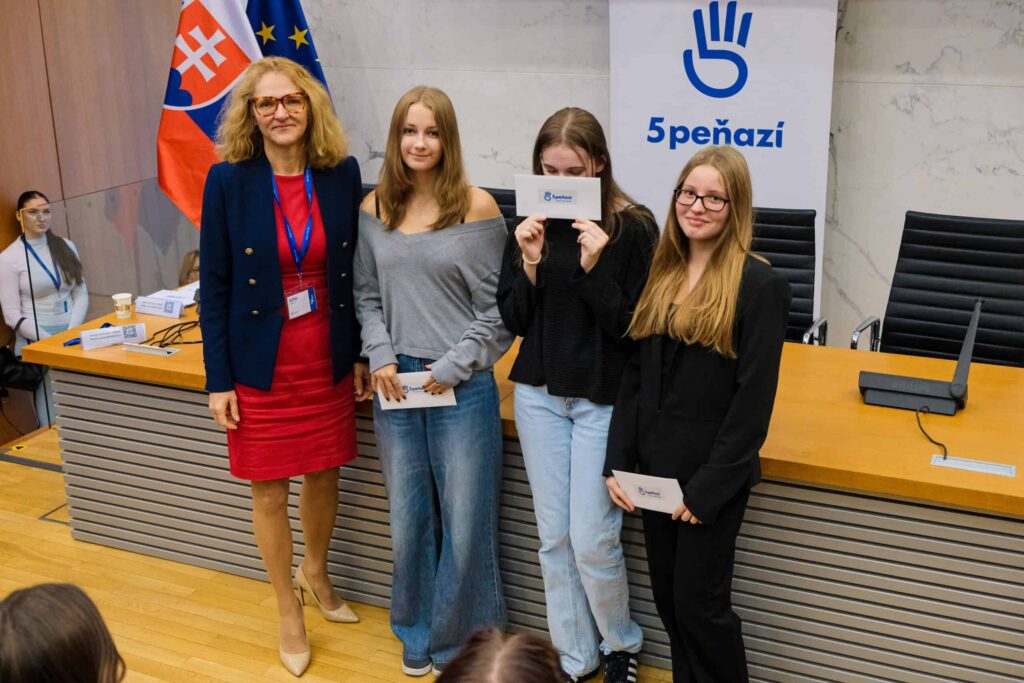 Štyri ženy stoja pred stolom a nápisom 5PEŇAZÍ. Tri mladé ženy držia certifikáty a vedľa nich stojí staršia žena v červených šatách a tmavomodrom saku. V pozadí je vidieť slovenskú vlajku.