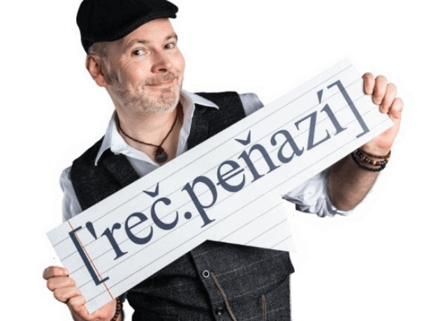 Usmievajúci sa muž v čiapke a veste drží nápis [reč.peňazí] napísaný veľkými písmenami s diakritikou, ktorý stojí na bielom pozadí.