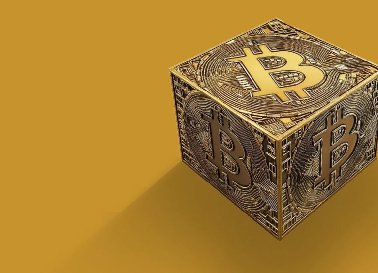 Zlatá kocka so symbolom Bitcoinu na každej viditeľnej strane sa nachádza na jednoduchom horčicovožltom pozadí a vrhá tieň doľava.