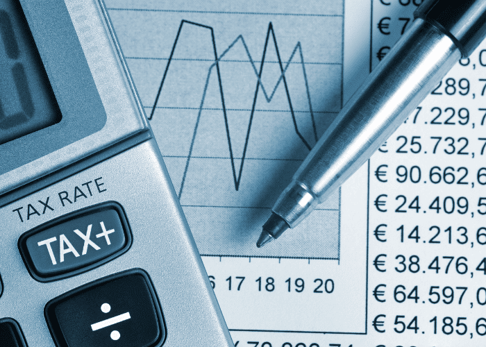 Záber zblízka na kalkulačku s tlačidlom TAX+, perom a finančným dokumentom zobrazujúcim sumy v eurách a čiarový graf, ktorý predstavuje finančné výpočty a analýzy.