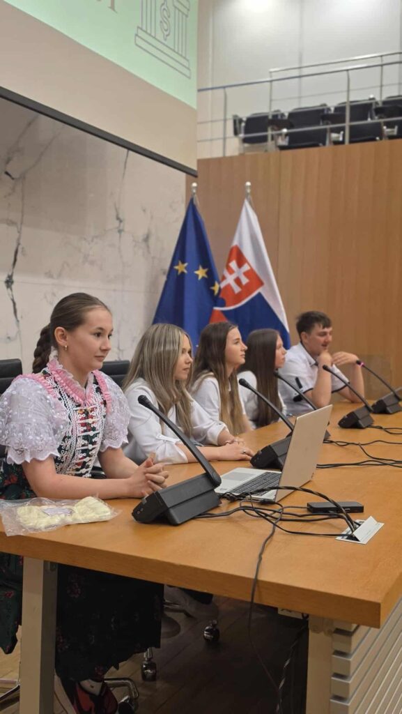 Päť mladých ľudí sedí pri konferenčnom stole s mikrofónmi počas finále Peňažného štvorboja v NBS.